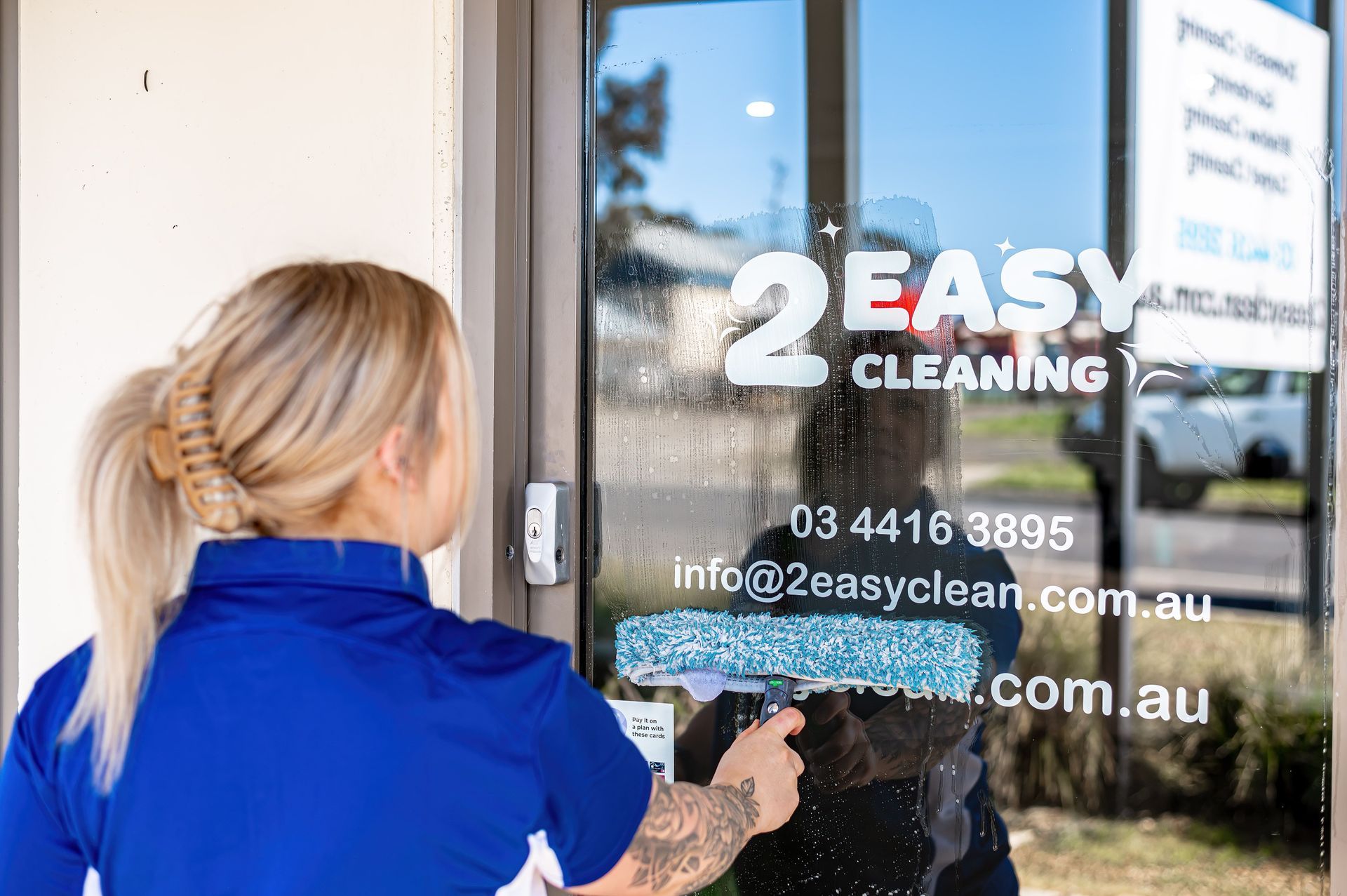 A Woman Is Cleaning A Glass Door With A Mop — 2easy Cleaning in Bendigo, VIC