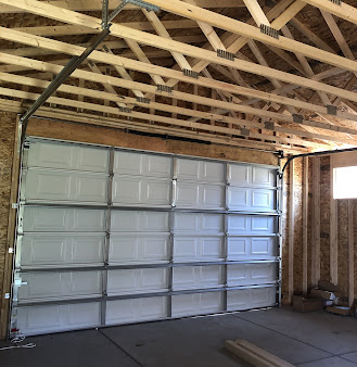 Interior of a garage under construction with an insulated white overhead door and exposed wooden roof framing