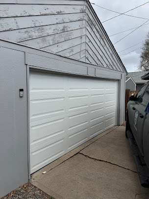White garage door beside a gray building and driveway, with a truck parked along the side