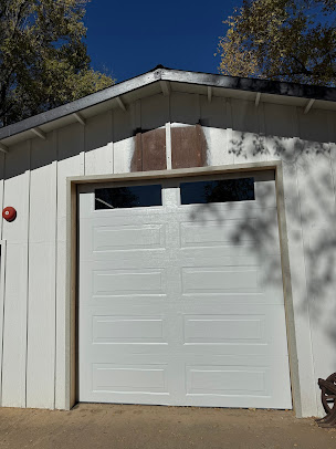 White garage door on a light beige building with two small windows above it, under a sloped roof.
