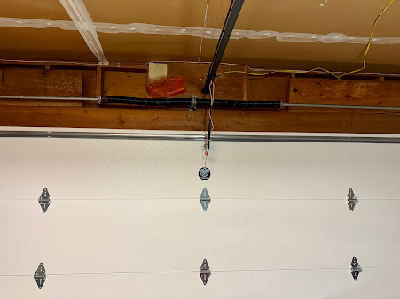 White garage door with metal hinges under exposed wooden ceiling beams and a hanging opener cord.
