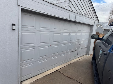 White garage door beside a parked dark pickup in a narrow driveway against light gray siding