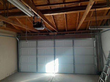 Empty garage interior with exposed wooden beams and closed white door, sunlight on concrete floor