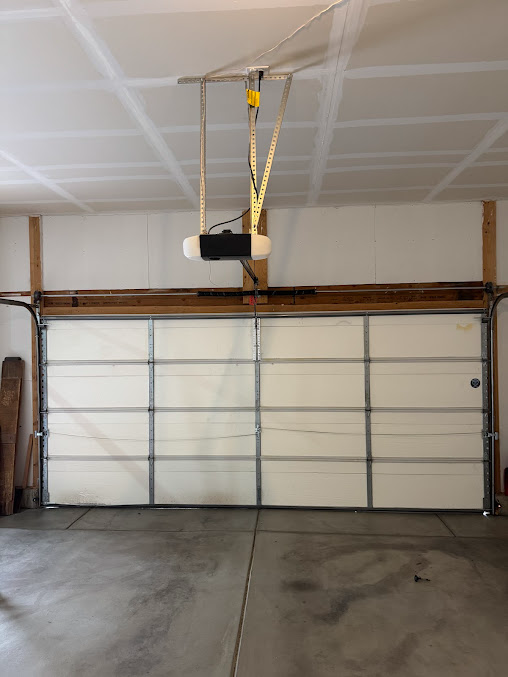 Garage interior with a closed sectional door and a ceiling-mounted garage door opener.