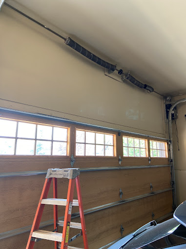Garage interior with red ladder, windows, ceiling door track, and part of a car visible.