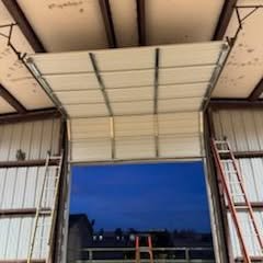 Interior of a metal building with a large open overhead door at dusk, ladders on both sides