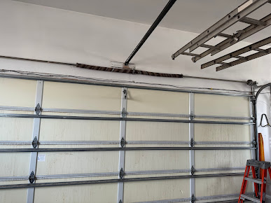 Inside a garage, a damaged sectional door with a bent top rail and a ladder on the right
