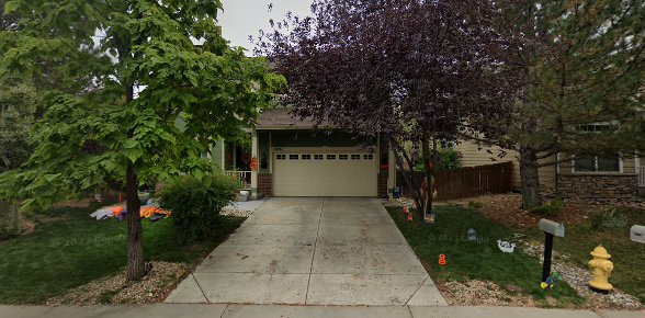 Suburban house with a two-car garage, driveway, trees, and a front yard with a yellow fire hydrant.