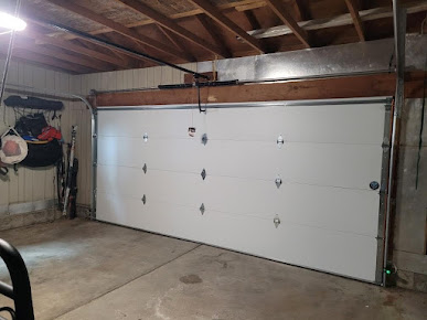 White garage door in a dim unfinished garage with exposed beams and concrete floor
