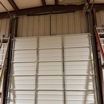 White metal garage door inside a warehouse, framed by corrugated metal walls.