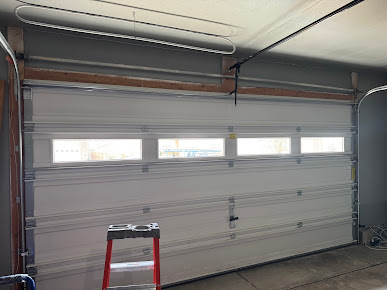 Closed white garage door with four windows, a red step ladder in front, and a garage door opener overhead