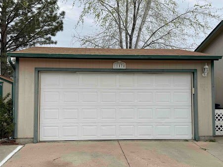 Single-car garage with a closed white door and beige exterior trim under trees