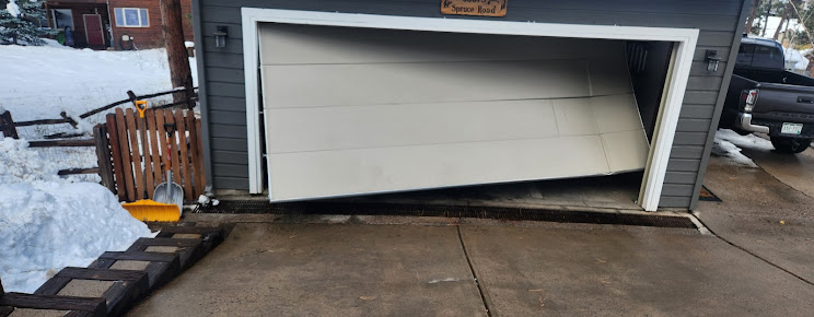 Collapsed garage door lying outward on a driveway beside snow and parked vehicles