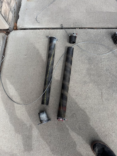Two black cylindrical rods with attached cables lying on a concrete sidewalk near a curb.