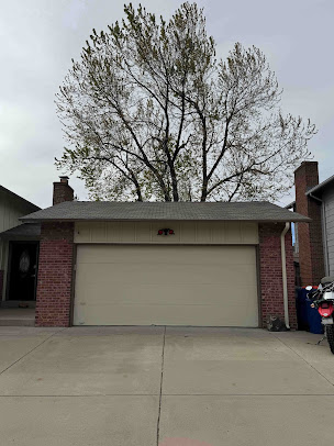 Suburban house with beige garage door, brick trim, and a large tree overhead