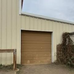 Tan metal roll-up door in a beige industrial building with vines on the right side.