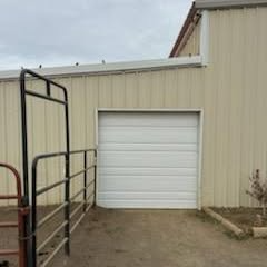 White roll-up garage door on beige metal building beside a paved driveway and black railings