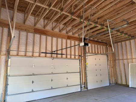 Empty garage interior with two white overhead doors and exposed wood framing