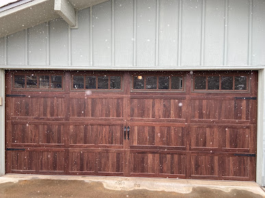 Brown wooden garage door on a house exterior with small window panels above.