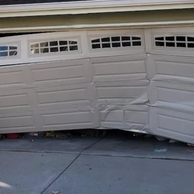 Damaged beige garage door bent inward at the bottom above a driveway