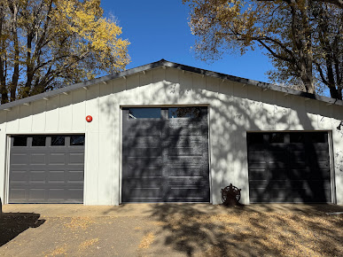 Three-car garage with white siding and black doors under autumn trees