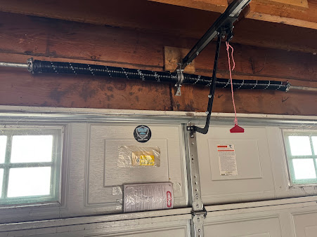 Interior of a garage with two windows, a white door, and exposed ceiling beams with hanging cables.