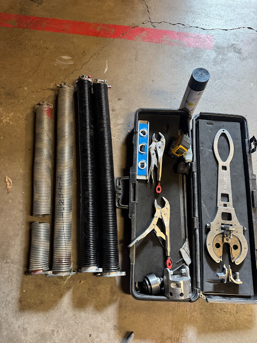 Assorted plumbing tools and coiled pipes laid out on a concrete floor.