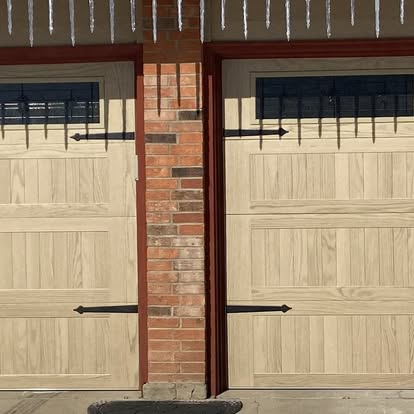 Two beige garage doors separated by a brick pillar under a covered carport.