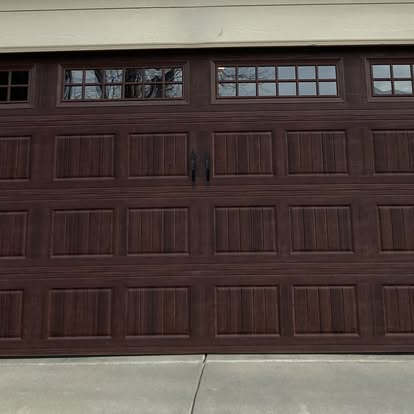 Dark brown wooden garage door with small windows above, set in a driveway.