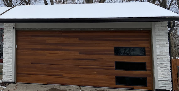 Wooden garage door with horizontal slats and four dark window panels, set in a snow-covered exterior.