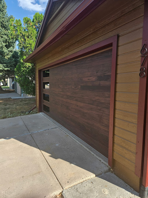 Wood-paneled garage door on a tan house beside a concrete driveway and trees