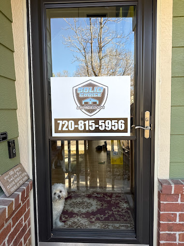 Front door with a phone-number sign, partially open to a hallway; small white dog visible inside.