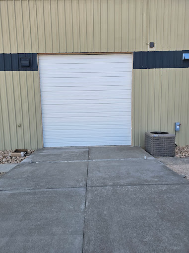 White roll-up garage door on a beige industrial building with concrete pavement in front.