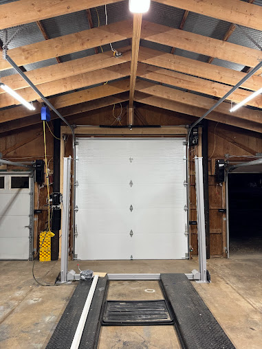 Garage interior with a white roll-up door, raised platform, and wooden rafters overhead