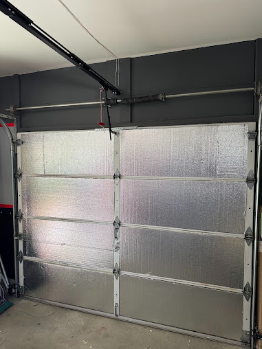 Silver insulated garage door with four panels in a dark-painted garage.