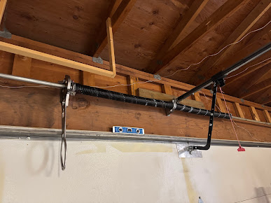 Garage ceiling with wooden rafters and a black garage door opener track above a wall-mounted level.