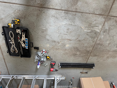 Assorted tools and black pipes laid out on a tiled floor next to a ladder