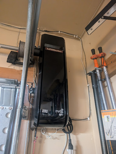 Black electrical panel mounted on beige wall beside metal pipes and orange clamps in a utility room