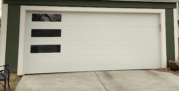 White garage door with three horizontal windows on a driveway, set in a green house exterior
