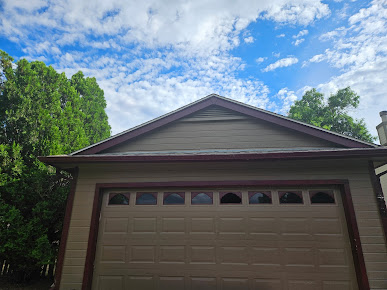 Garage with brown door and green trees under a bright blue, partly cloudy sky