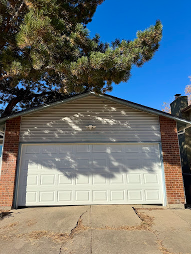 White garage door on a brick house with a tree casting shadows over the roof and driveway.