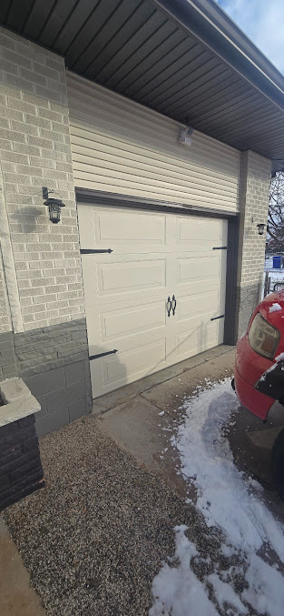 Exterior view of a white garage door on a brick house with snow on the ground and a red vehicle at right