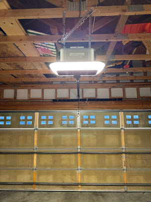 Garage door with a bright overhead opener light and exposed wooden ceiling beams above.