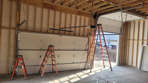 Unfinished garage interior with exposed framing, white door panels, and ladders leaning against the wall