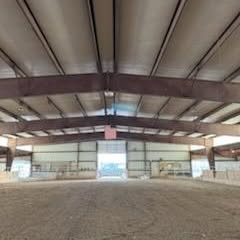 Interior of an empty indoor riding arena with a dirt floor and metal roof beams