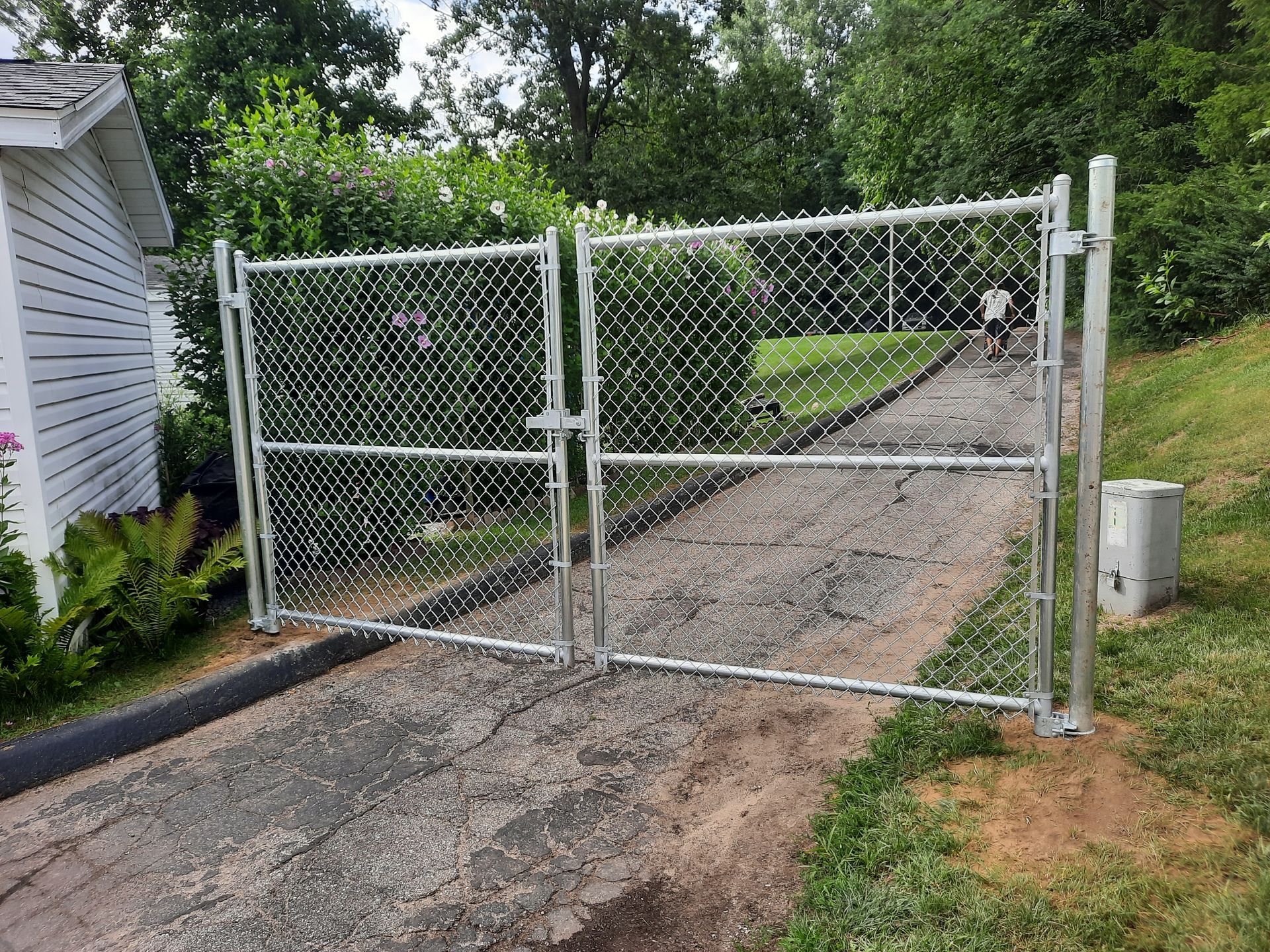 A chain link fence is surrounding a driveway leading to a house.