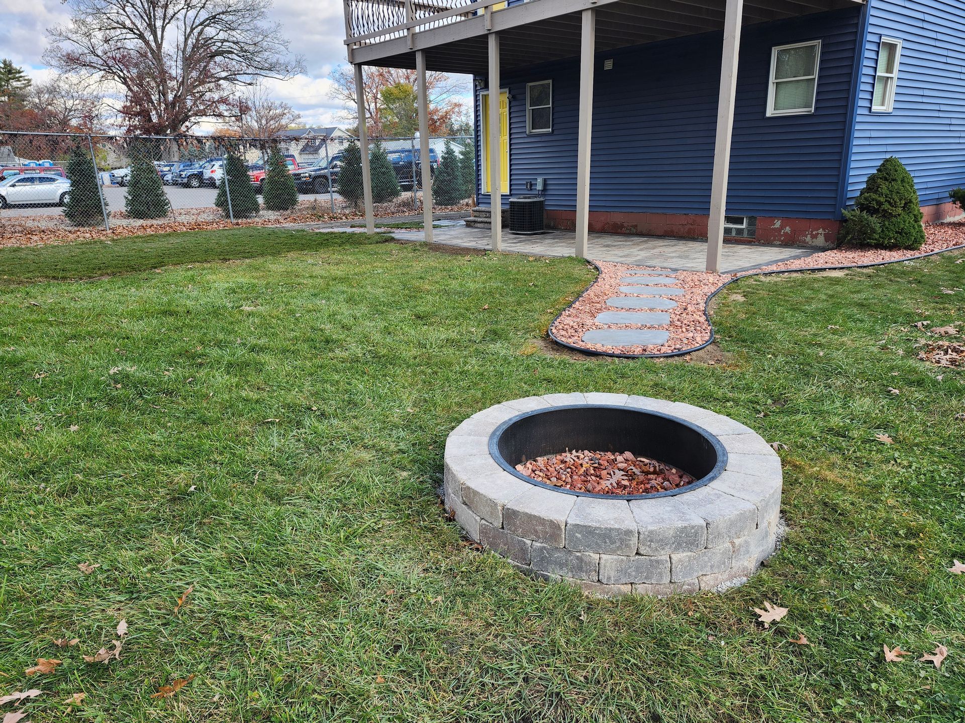 A fire pit is in the middle of a lush green lawn in front of a house.