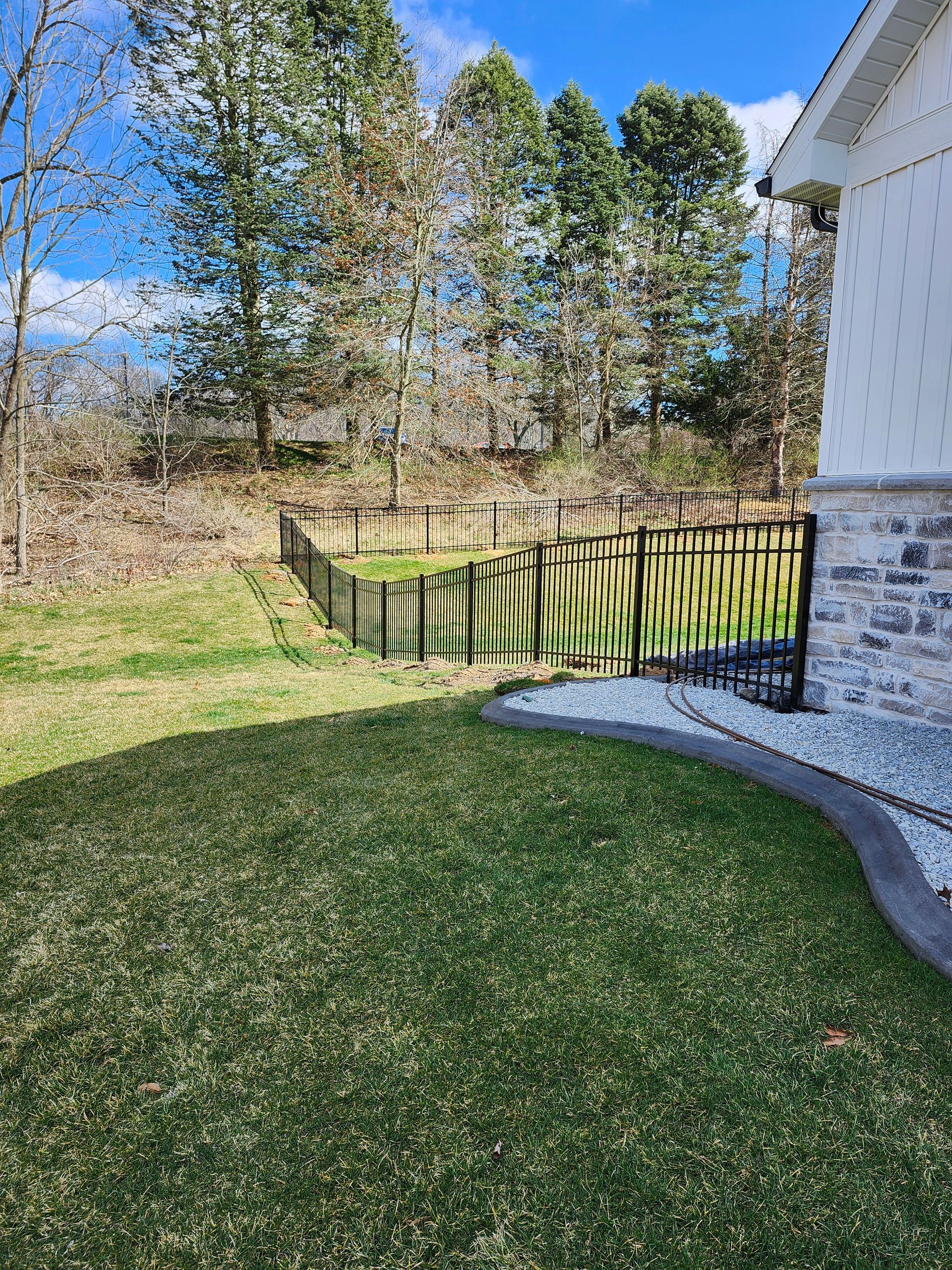 A fence surrounds a lush green lawn in front of a house.