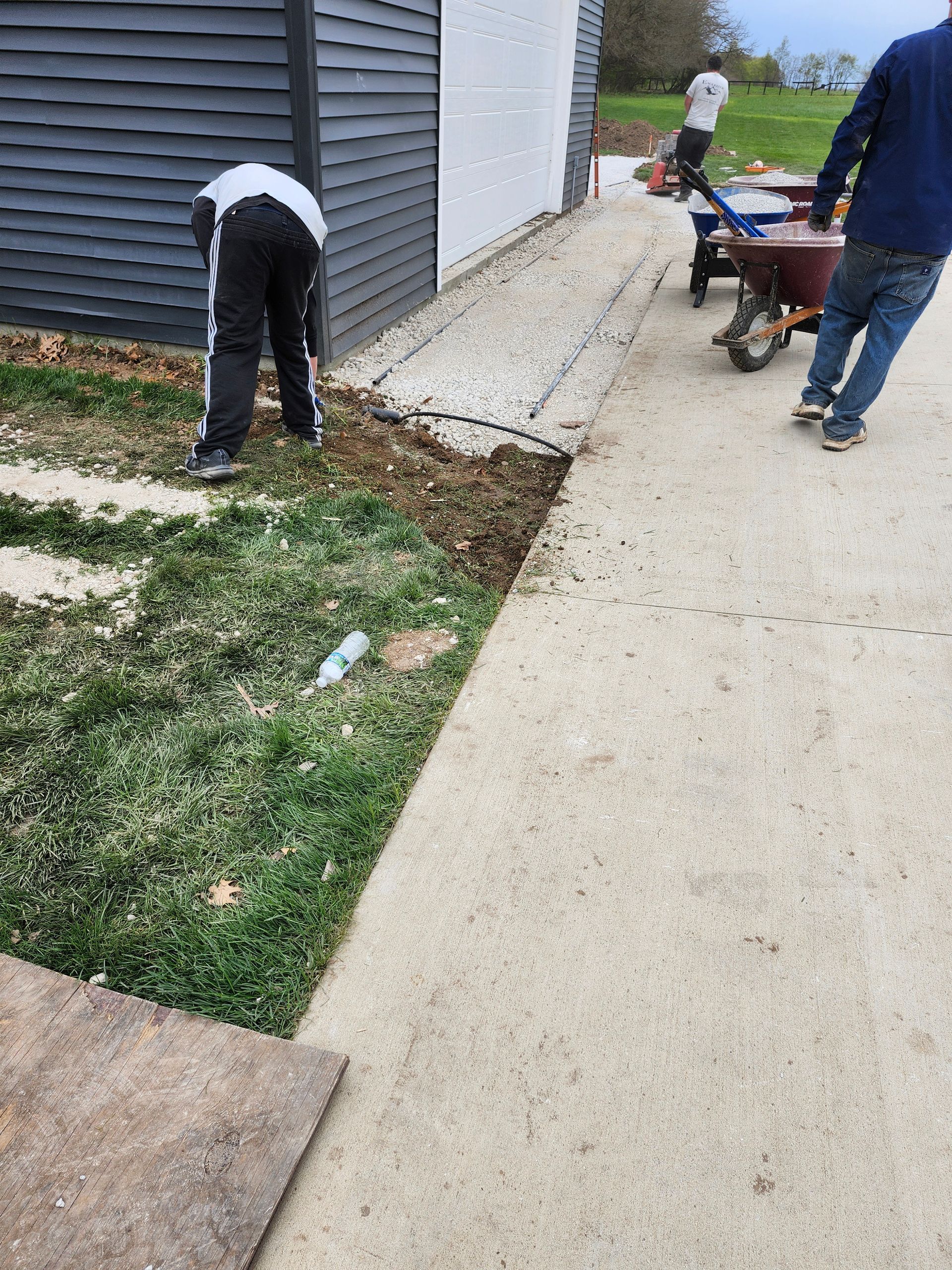 A man is standing in the grass next to a wheelbarrow.