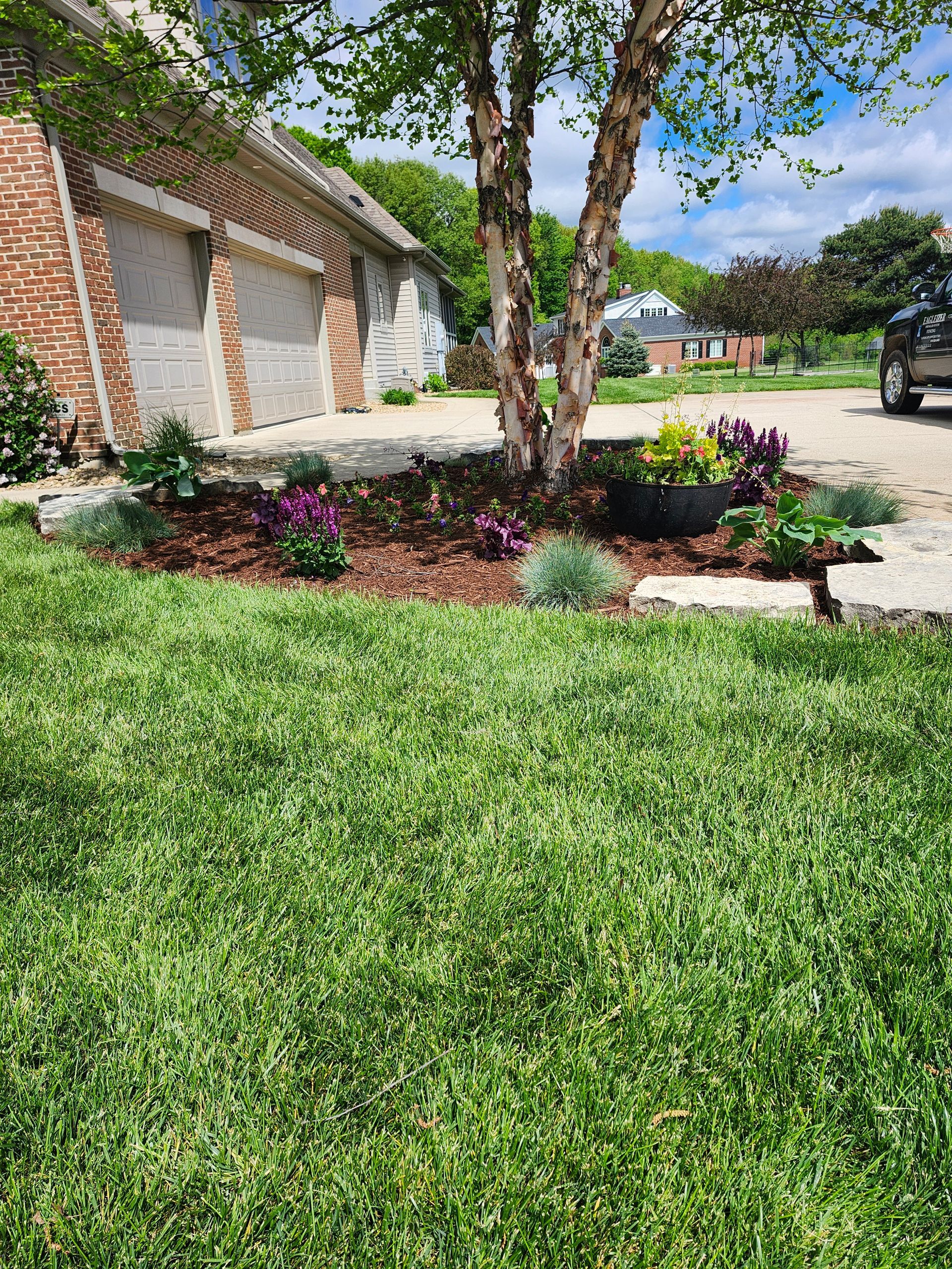 A lush green lawn with flowers and a tree in front of a house.